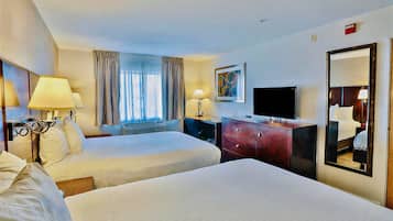 Una habitación de hotel con dos camas, televisión, cómoda y ventana con cortinas.