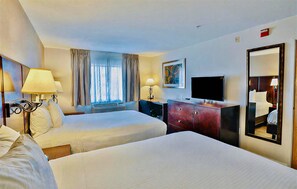 Una habitación de hotel con dos camas, televisión, cómoda y ventana con cortinas.