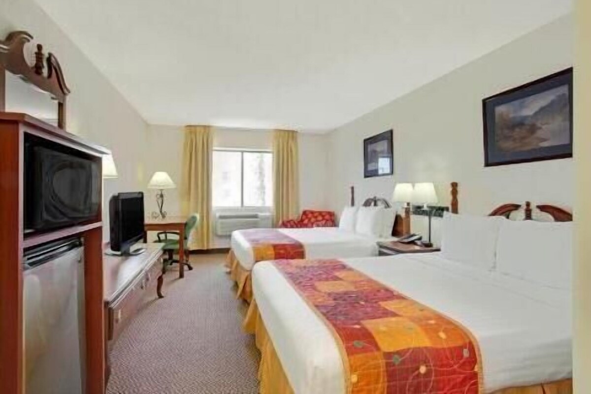 A hotel room with two beds, a desk, a television, and a window with curtains.