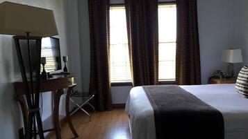 A hotel room with a bed, a desk with a computer, a chair, a lamp, and a window with curtains.