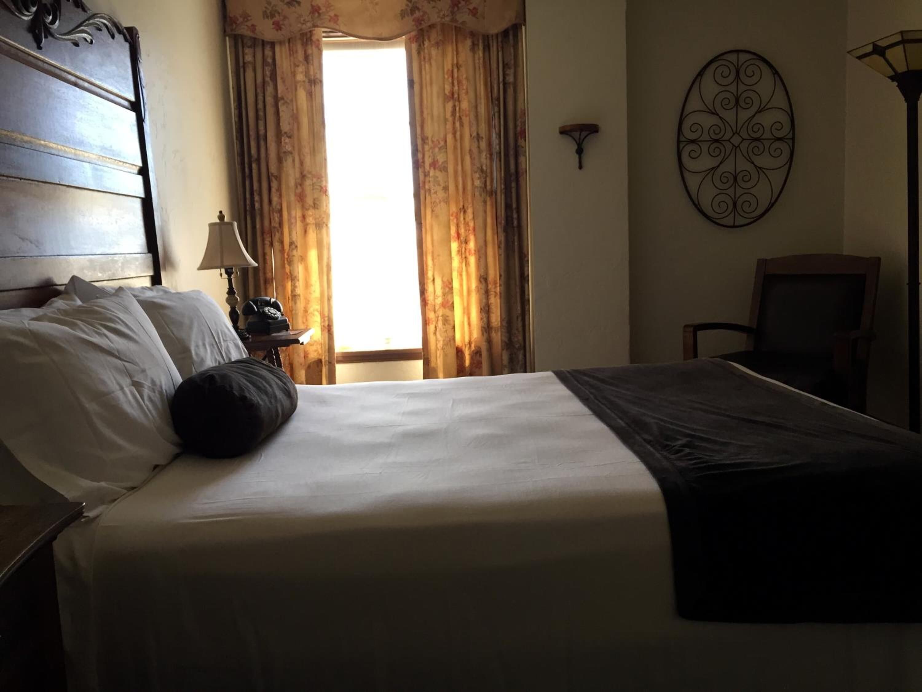 Una habitación de hotel con una cama grande, una mesita de noche con lámpara, una silla y un adorno en la pared.