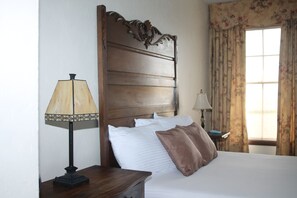 Una cama bien hecha con almohadas blancas y marrones, un cabecero de madera y dos mesitas de noche con lámparas.