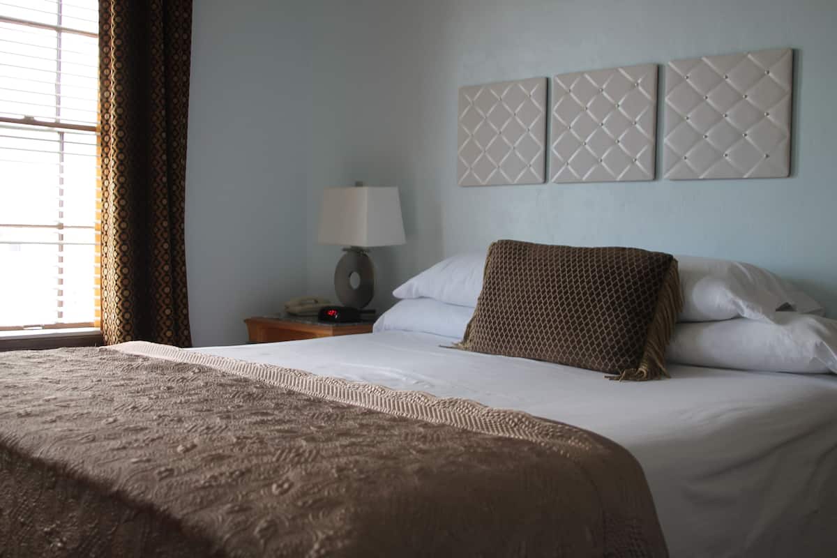 A hotel room with a large bed, a bedside table with a lamp, and a window with curtains.