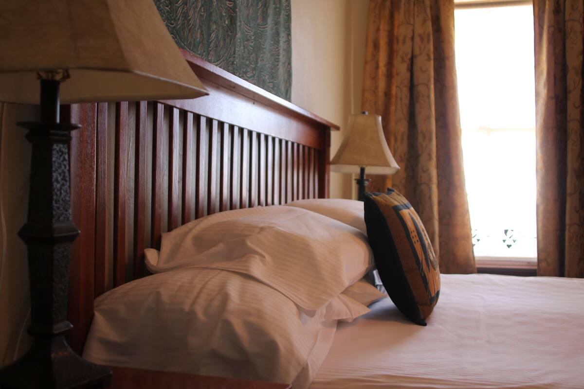 A neatly made bed with white linens, a wooden headboard, and a lamp on the nightstand.