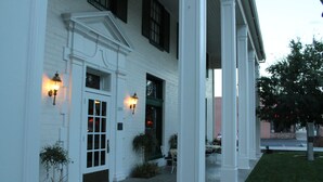 A white building with a covered entrance, a door with glass panels, and two wall-mounted lights. - Boulder Dam Hotel (Boulder City)