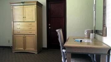 A room with a wooden cabinet, a dark door, a table with a chair, and a mirror on the wall.