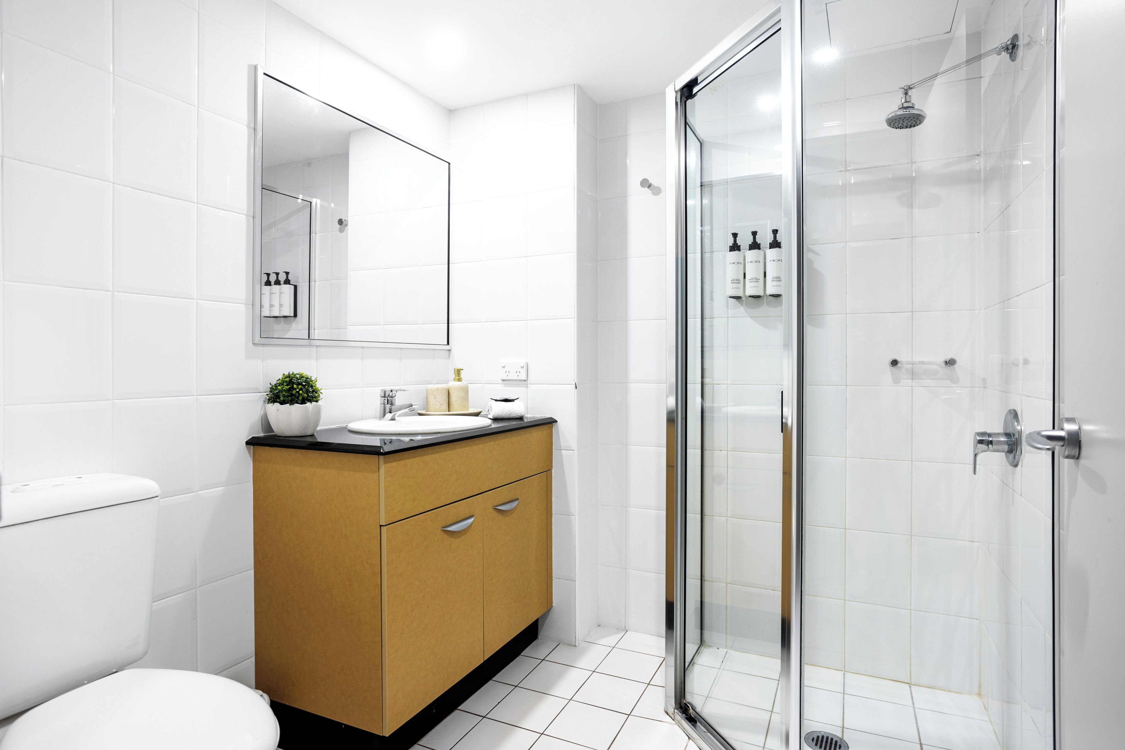Un baño moderno con cabina de ducha de vidrio, inodoro blanco y tocador de madera con espejo.