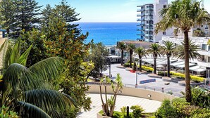 A coastal hotel with a view of the sea, palm trees, and modern architecture.