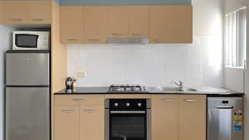 A modern kitchen with beige cabinets, a stainless steel refrigerator, a microwave, a gas stove, and a dishwasher.