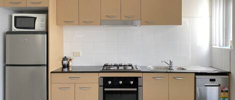 A modern kitchen with beige cabinets, a stainless steel refrigerator, a microwave, a gas stove, and a dishwasher.