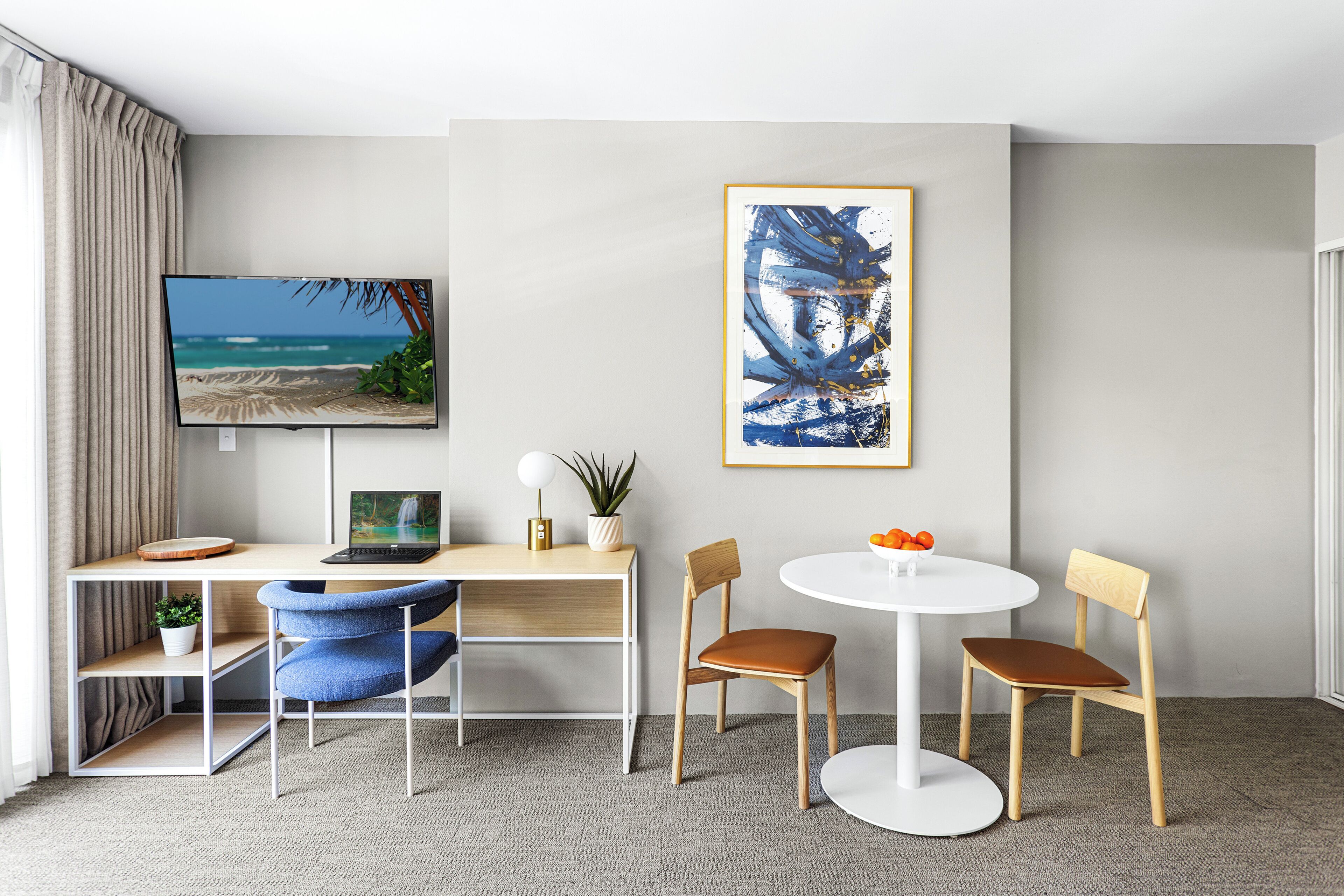 A modern room with a desk, two chairs, a round table, a TV, and artwork on the wall.