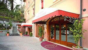 A hotel entrance with a red awning, a red carpet, and potted plants. - Alla Rocca Hotel (Valsamoggia)