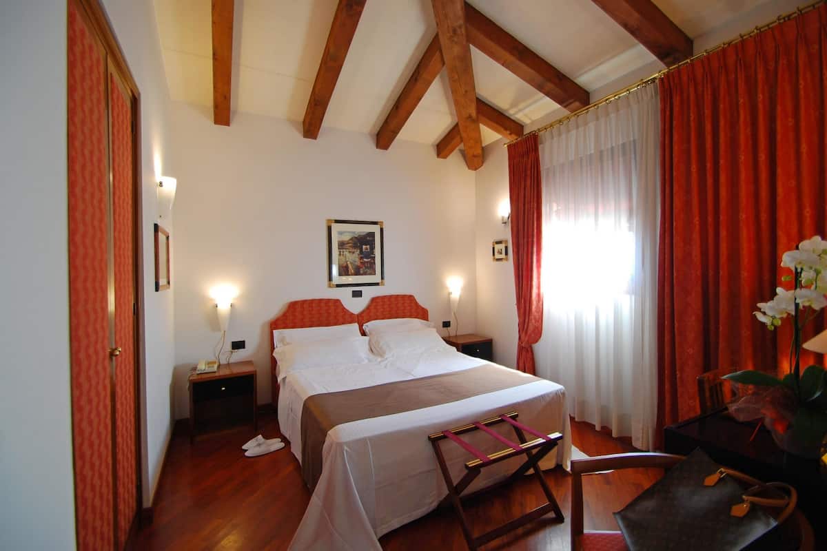A bedroom with a bed, wooden beams, a nightstand, a chair, and a desk with a lamp.