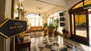 A hotel lobby with a checkered floor, a sofa, a coffee table, potted plants, and a sign reading "HOTEL ALLA ROCCA". - Alla Rocca Hotel (Valsamoggia)