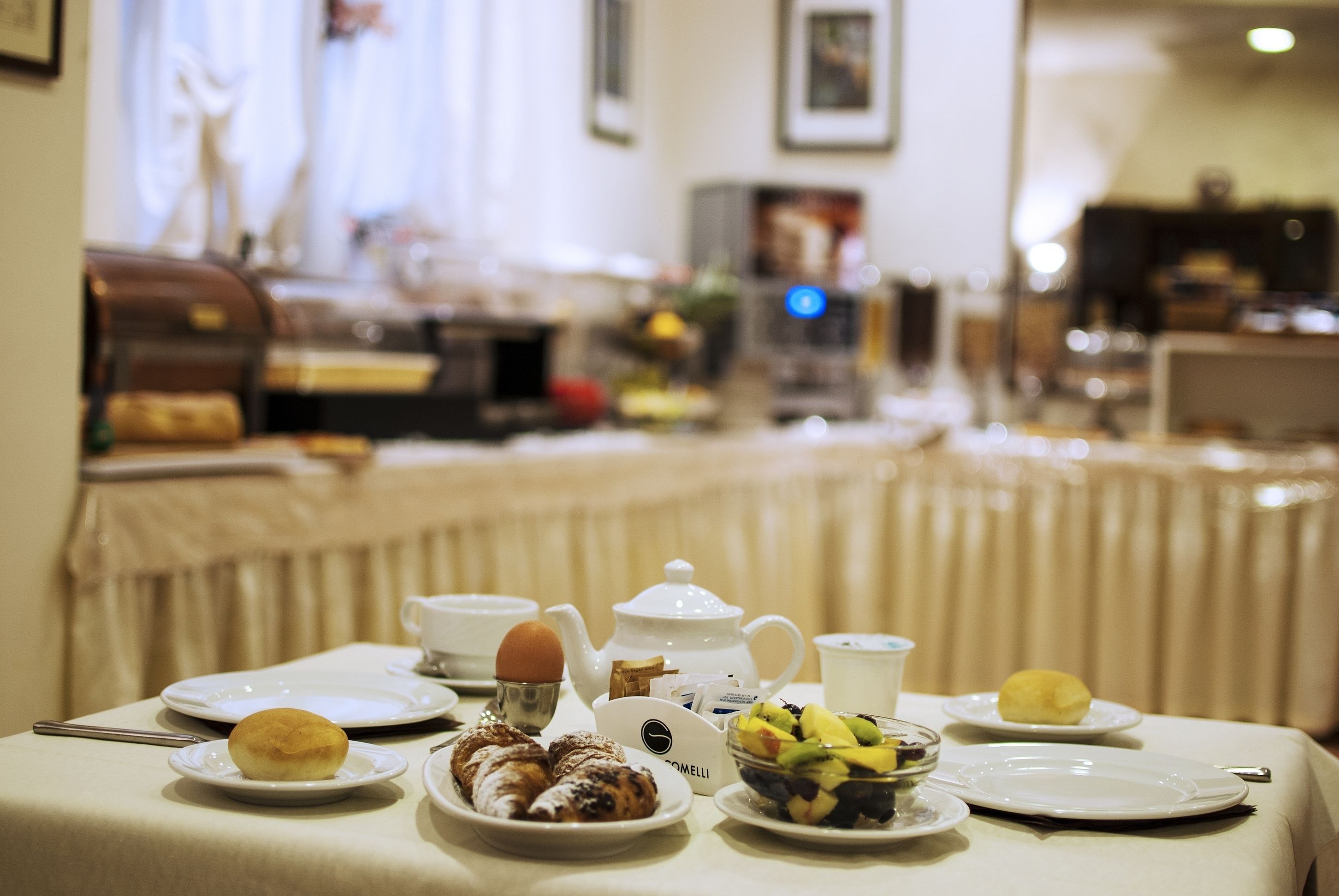 A breakfast table set with plates, a teapot, and various pastries and fruits.