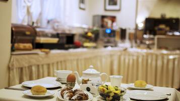 A breakfast table set with plates, a teapot, and various pastries and fruits.