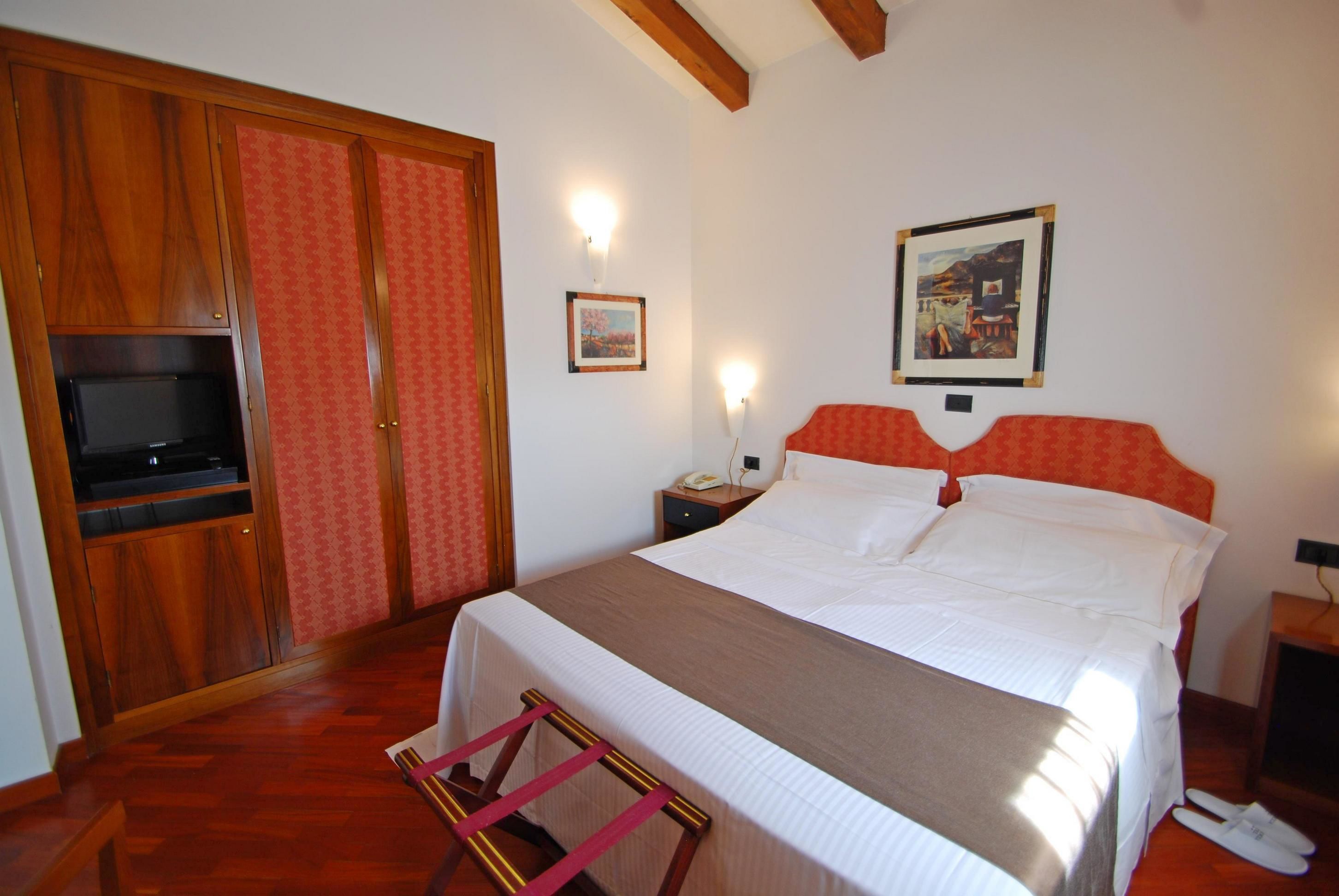 A hotel room with a bed, wooden wardrobe, and a television.