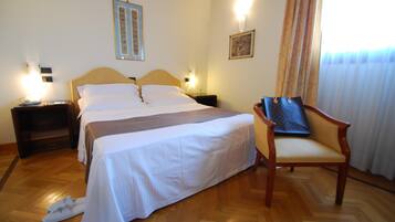 Une chambre d’hôtel avec un grand lit, deux tables de chevet, une chaise et une fenêtre avec des rideaux.