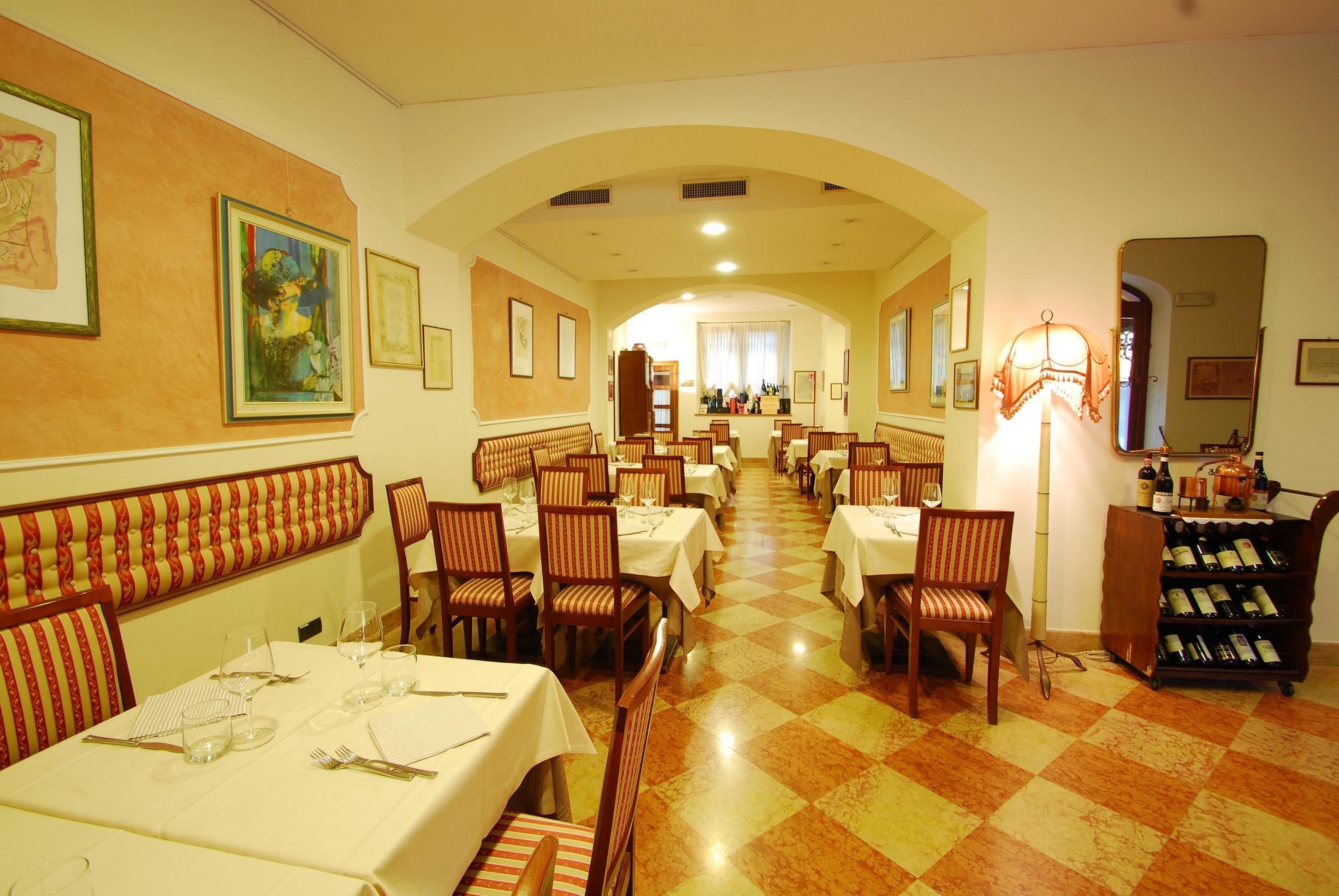 A restaurant with multiple tables and chairs, a wine rack, and framed artwork on the walls.