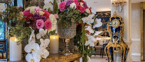 Un lobby lujoso con decoración elaborada, que incluye un reloj imponente y un arreglo floral sobre una mesa de mármol.