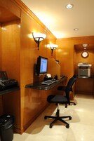 Ett hotellrum med en väggpanel av trä, ett skrivbord med en dator, en stol, en papperskorg och en klocka på väggen.