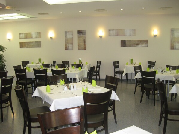 A dining area with multiple tables and chairs, each set with white tablecloths and green napkins.