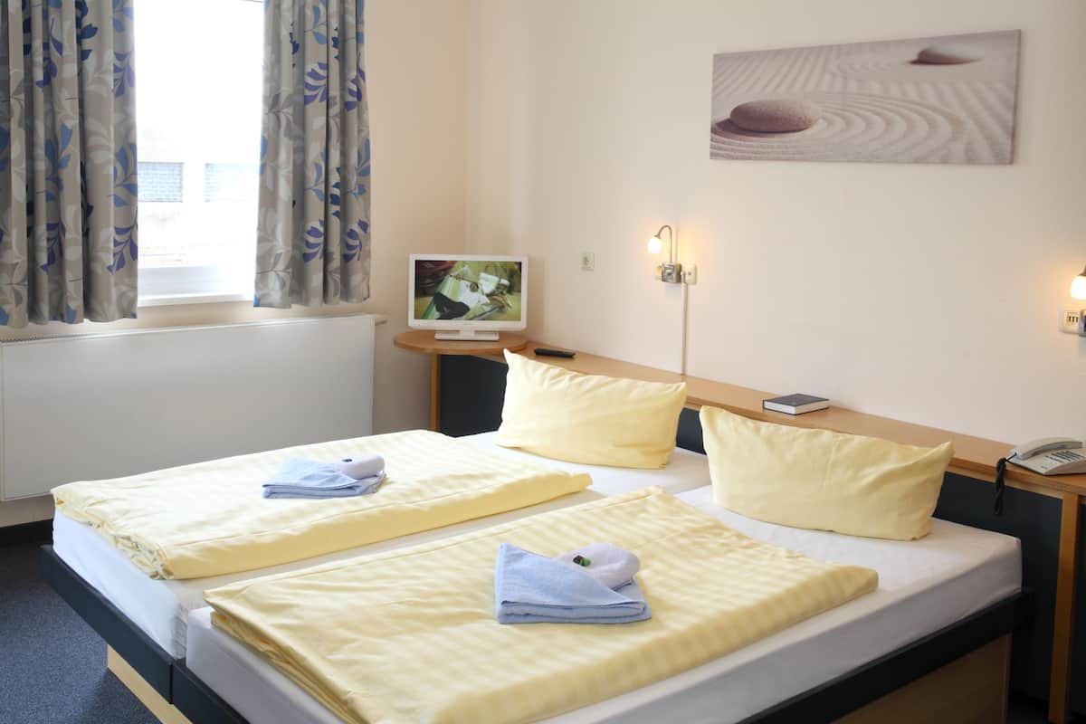 Ein Hotelzimmer mit zwei Betten, einem Flachbildfernseher, einer Nachttischlampe und einem Bild an der Wand.