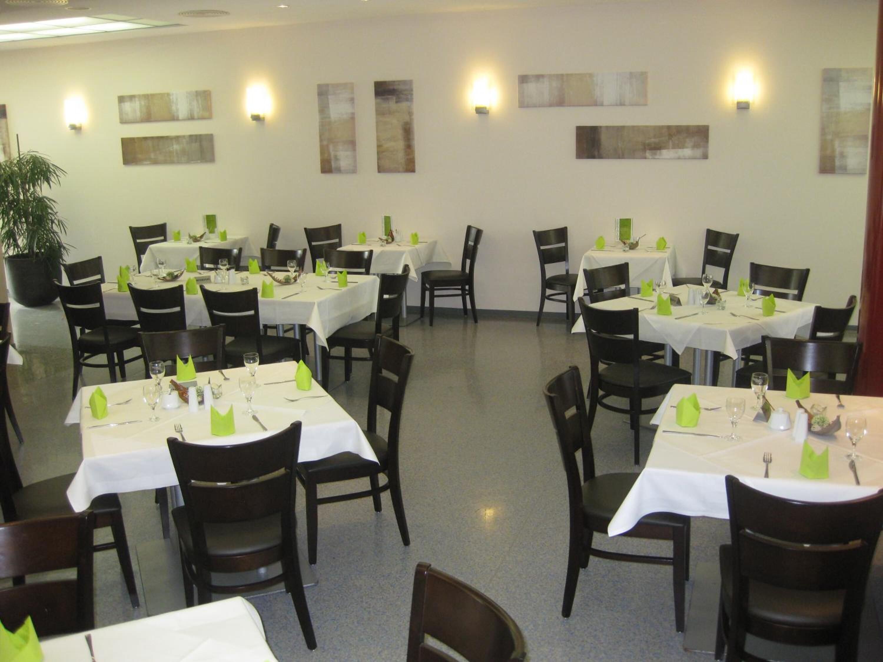 A restaurant with multiple tables and chairs, each set with white tablecloths and green napkins.