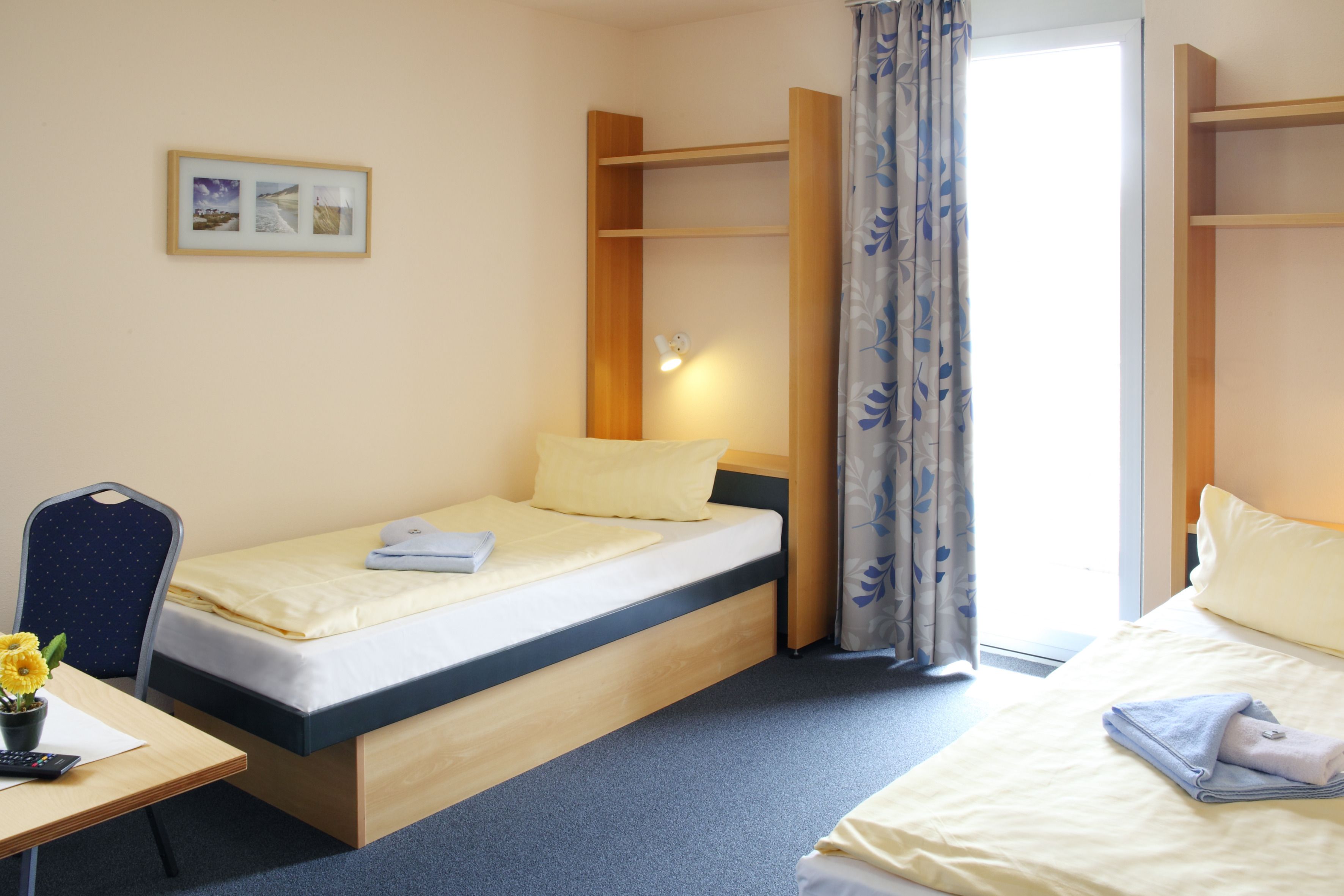 Una habitación de hotel compacta con una cama individual, un escritorio con una silla y una mesita con un florero.