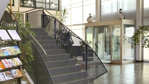 A spacious lobby with a staircase, large windows, and a reception area.