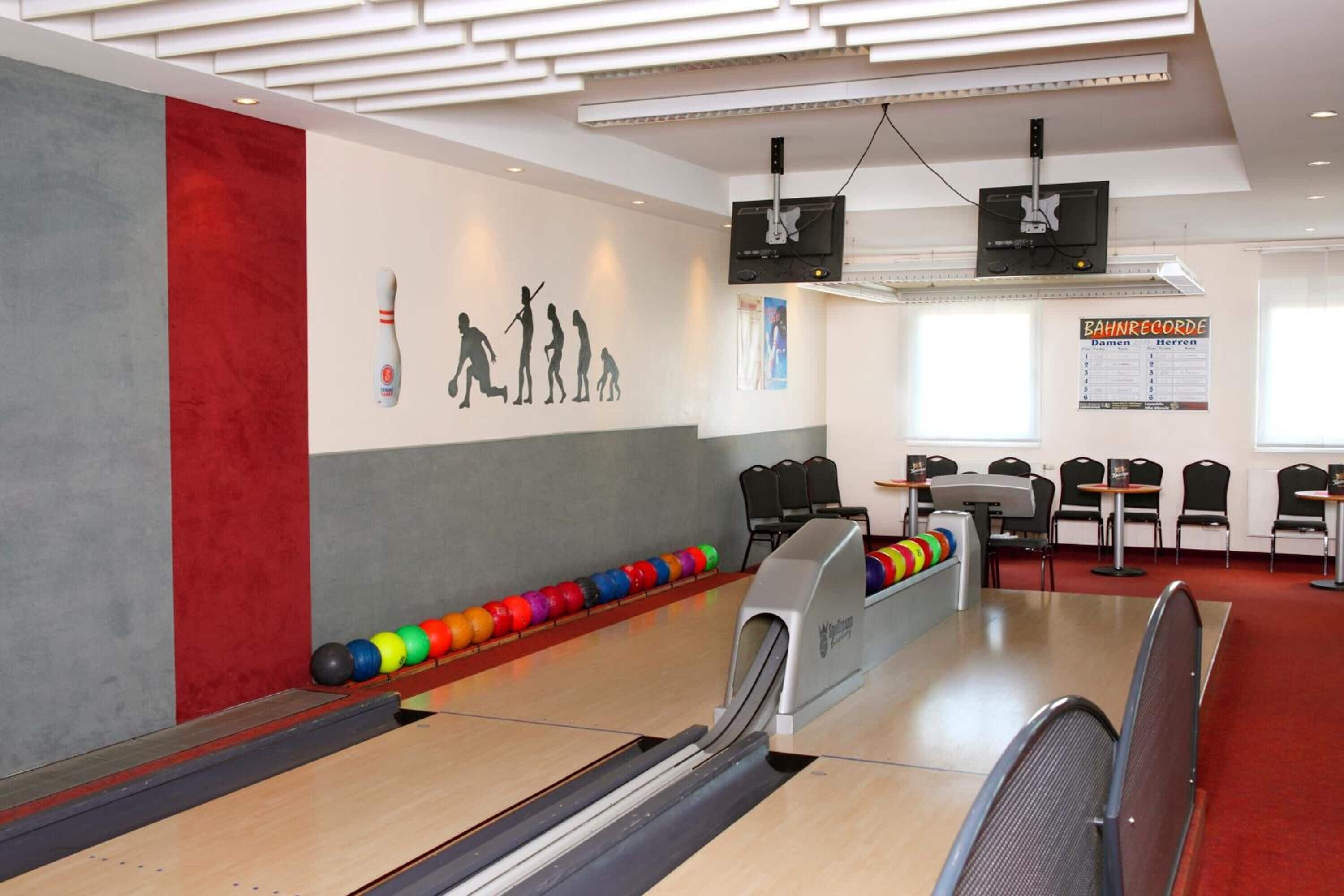 A bowling alley with a red and grey wall, a bowling ball rack, and a scoreboard.