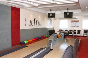En bowlinghall med en röd och grå vägg, ett ställ för bowlingklot och en resultattavla.