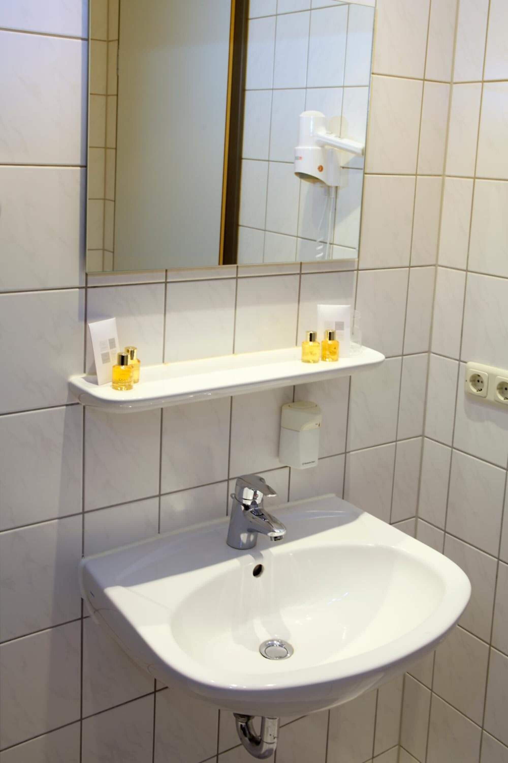 A bathroom with a white sink, a mirror, and a shelf with toiletries.