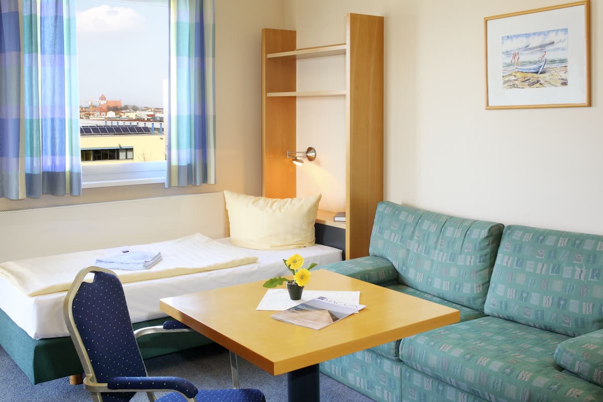 Ein Hotelzimmer mit Bett, einer Couch, einem Tisch mit Blumenvase und einem Fenster mit Vorhängen.