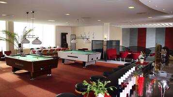 A pool table, bar area with stools, and red chairs in a well-lit room with large windows.