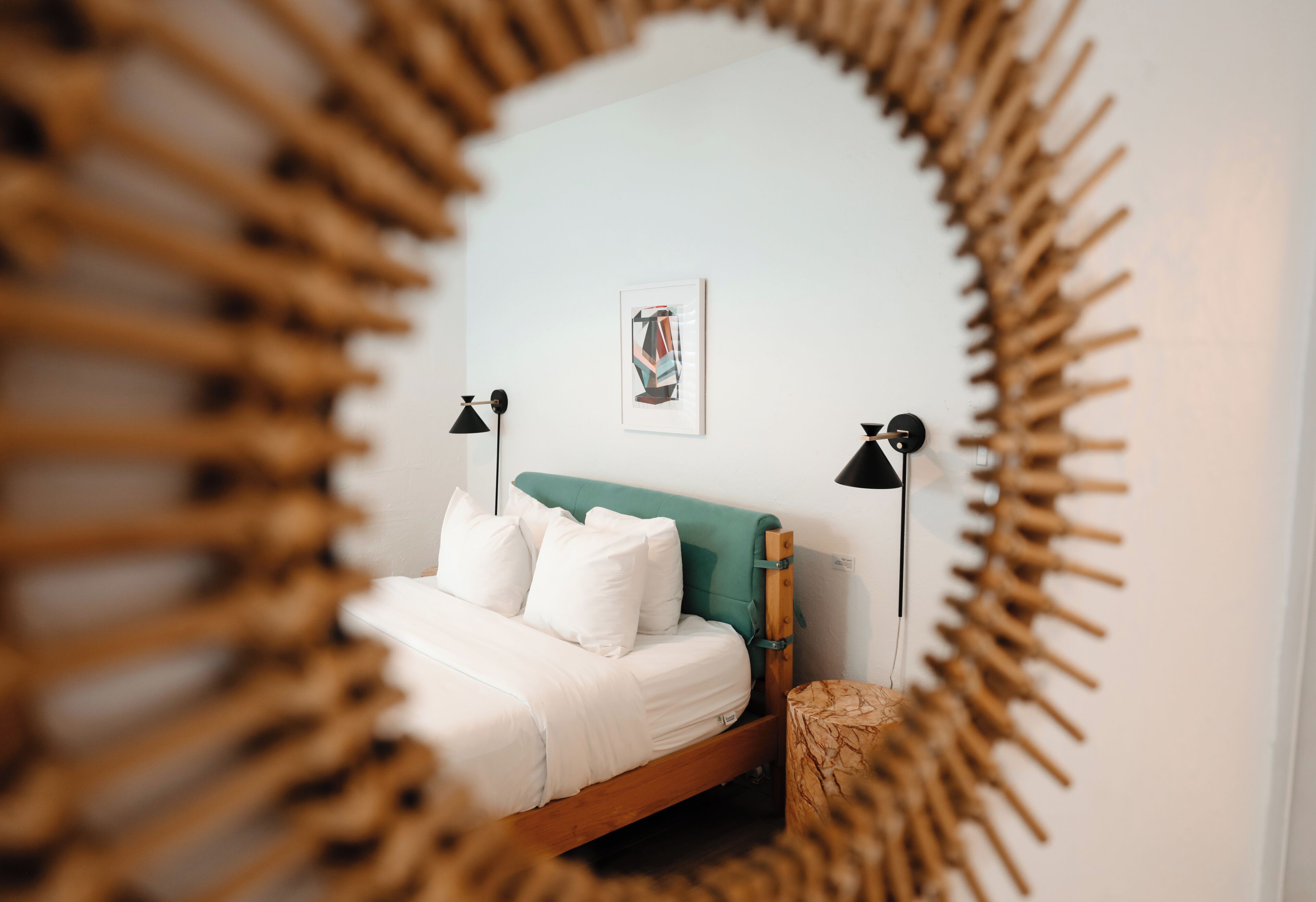 Una cama con ropa de cama blanca, un cabecero verde azulado y dos lámparas de noche.