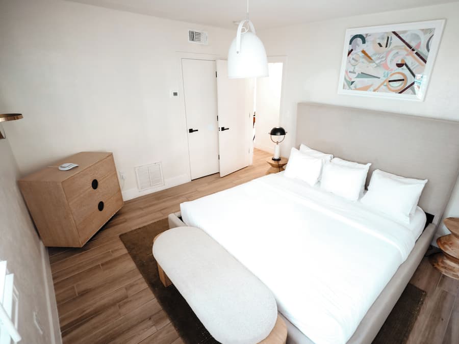 Ein modernes Schlafzimmer mit einem großen Bett, einem Nachttisch, einer hölzernen Kommode und einer Pendelleuchte.