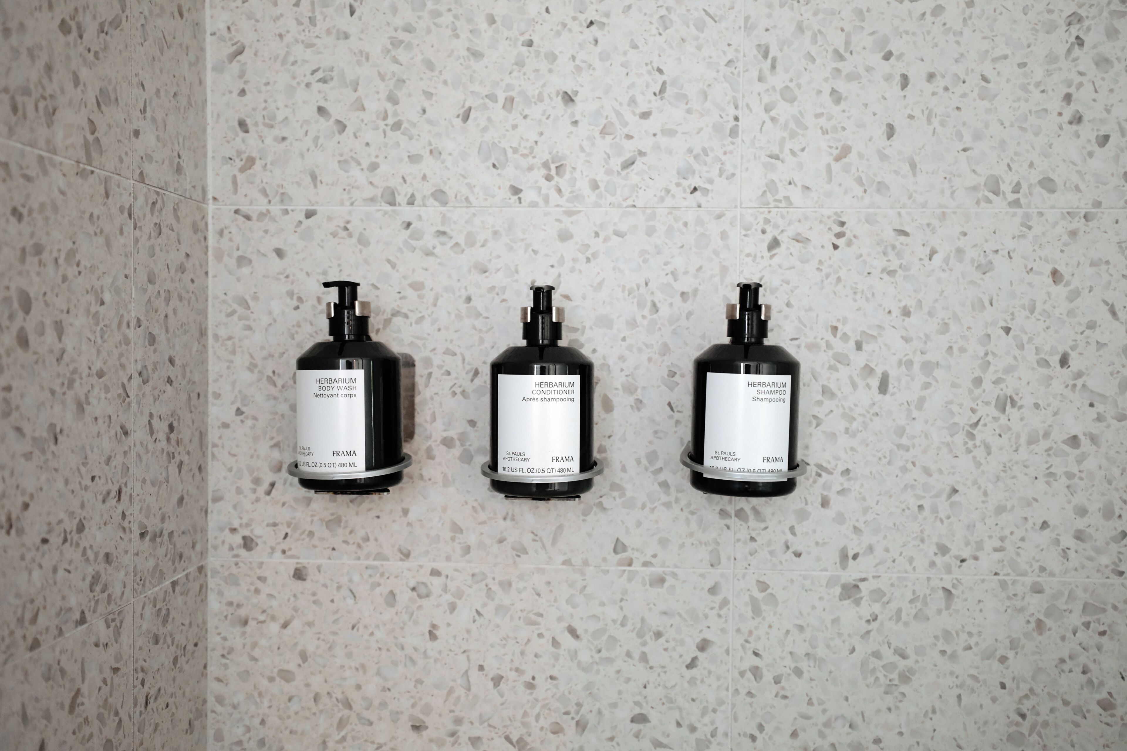 Three black bottles with labels on a speckled tile wall.