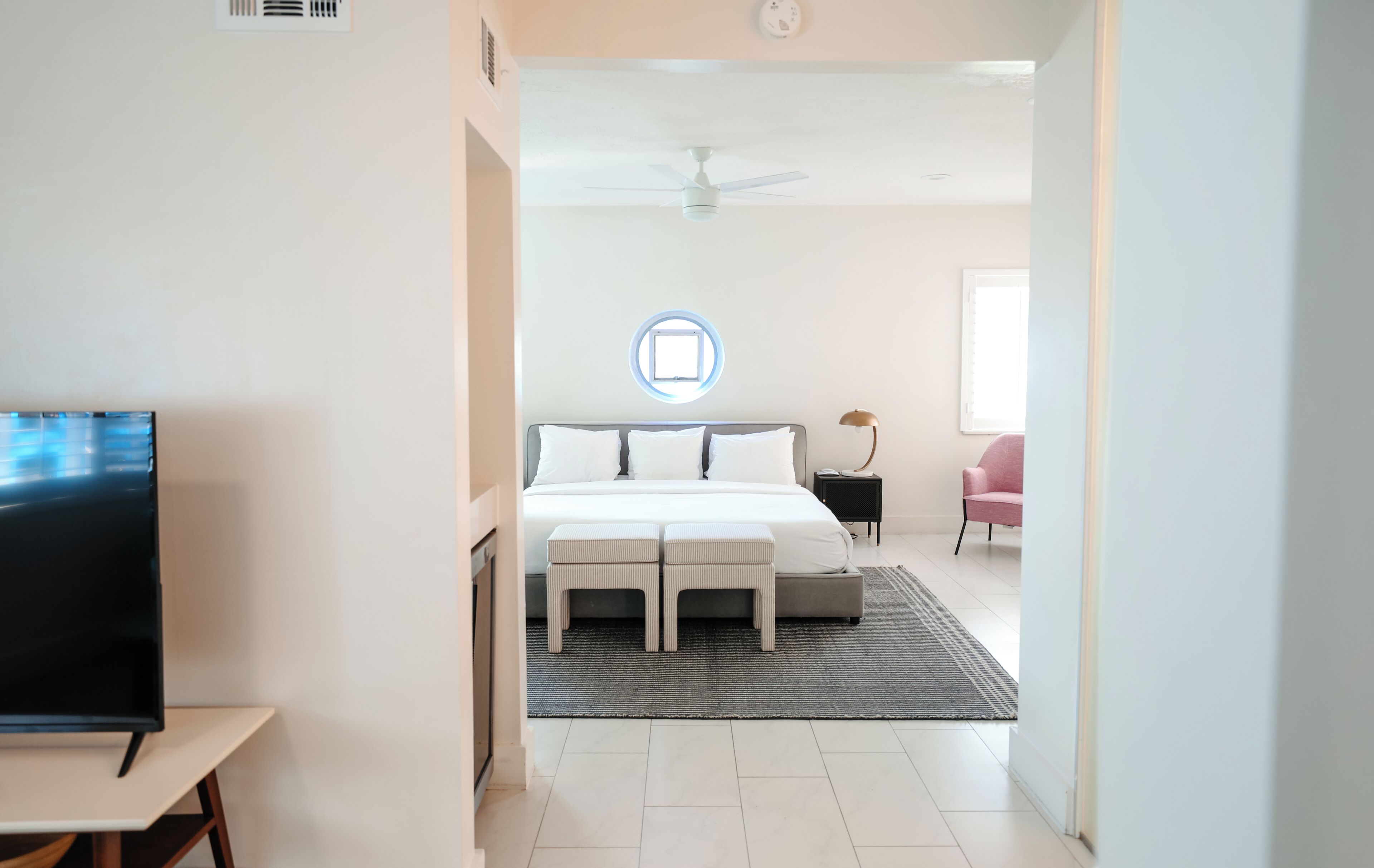 A modern hotel room with a bed, bedside table, TV, and a view of the hallway.