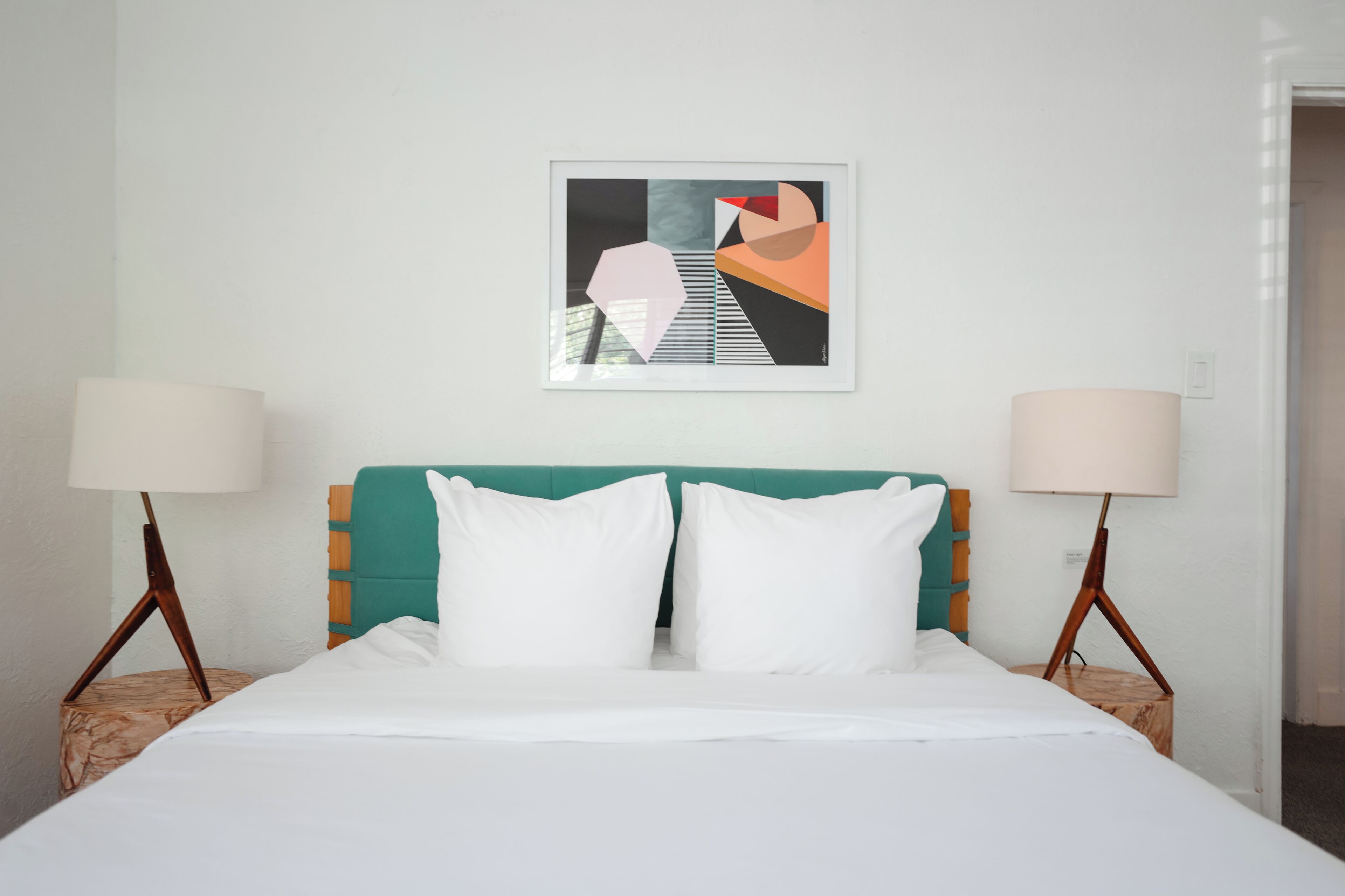 A bed with white bedding, a teal headboard, and two bedside lamps.