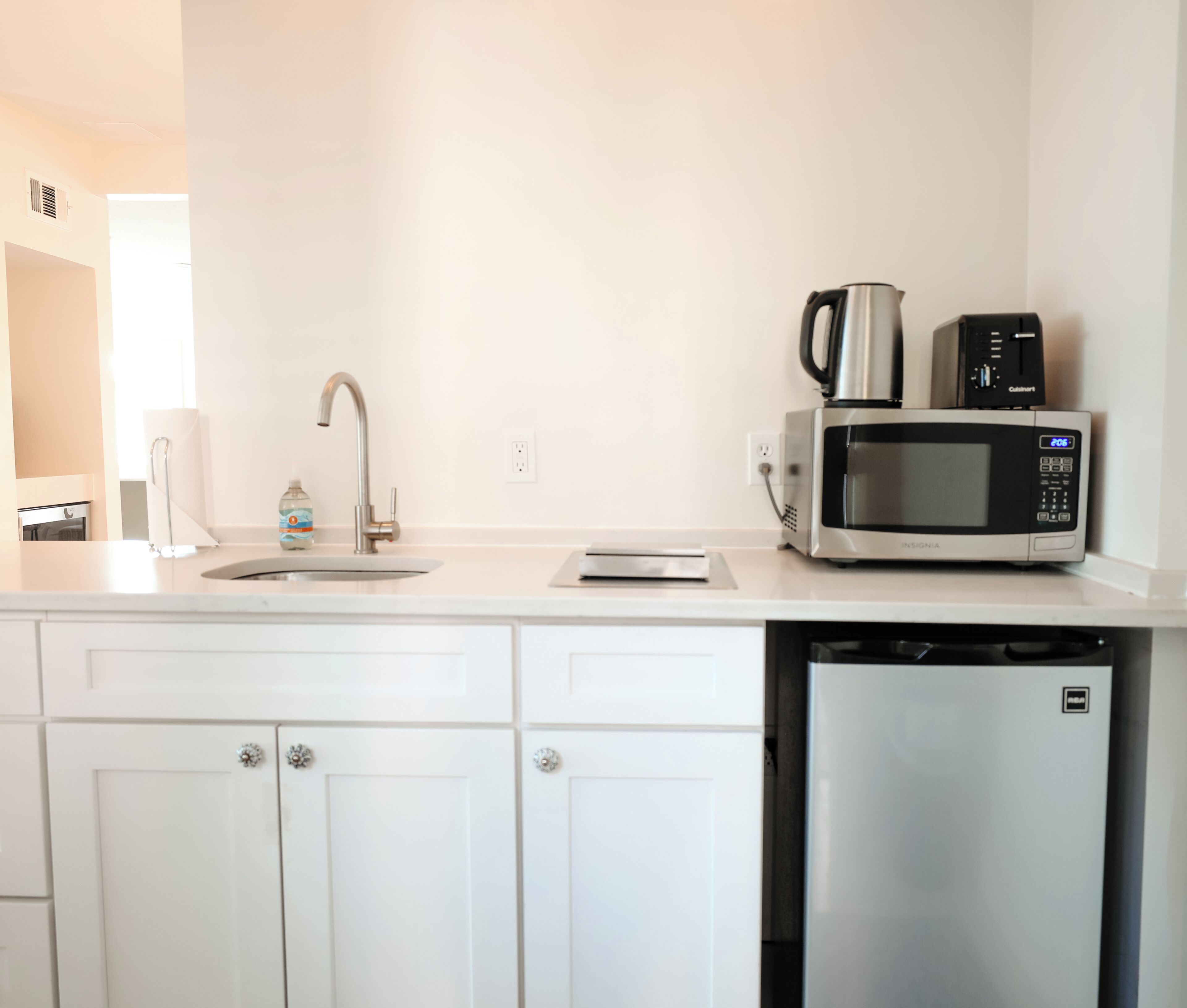 A compact kitchen with a sink, a coffee maker, a microwave, and a dishwasher.