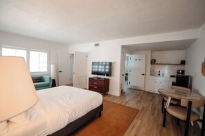 Una habitación de hotel con cama, televisión, escritorio y kitchenette.