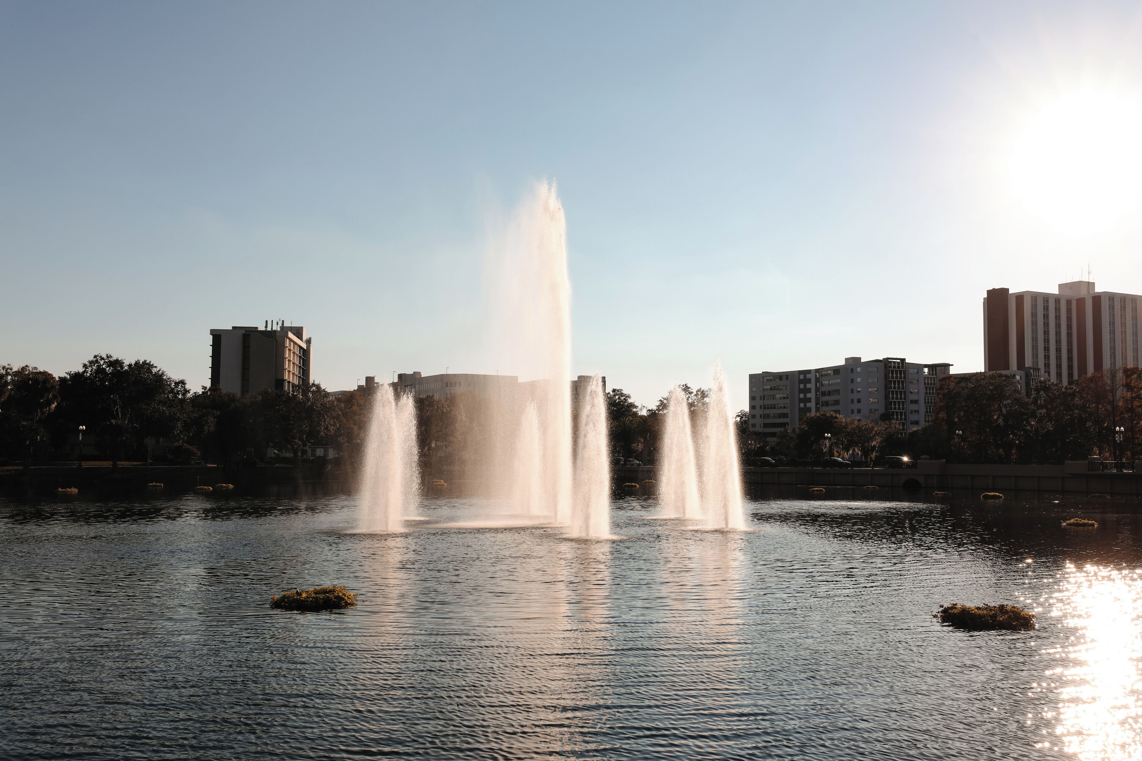 Une fontaine avec de nombreux jets d’eau, située dans un bassin, et entourée de bâtiments et d’arbres.