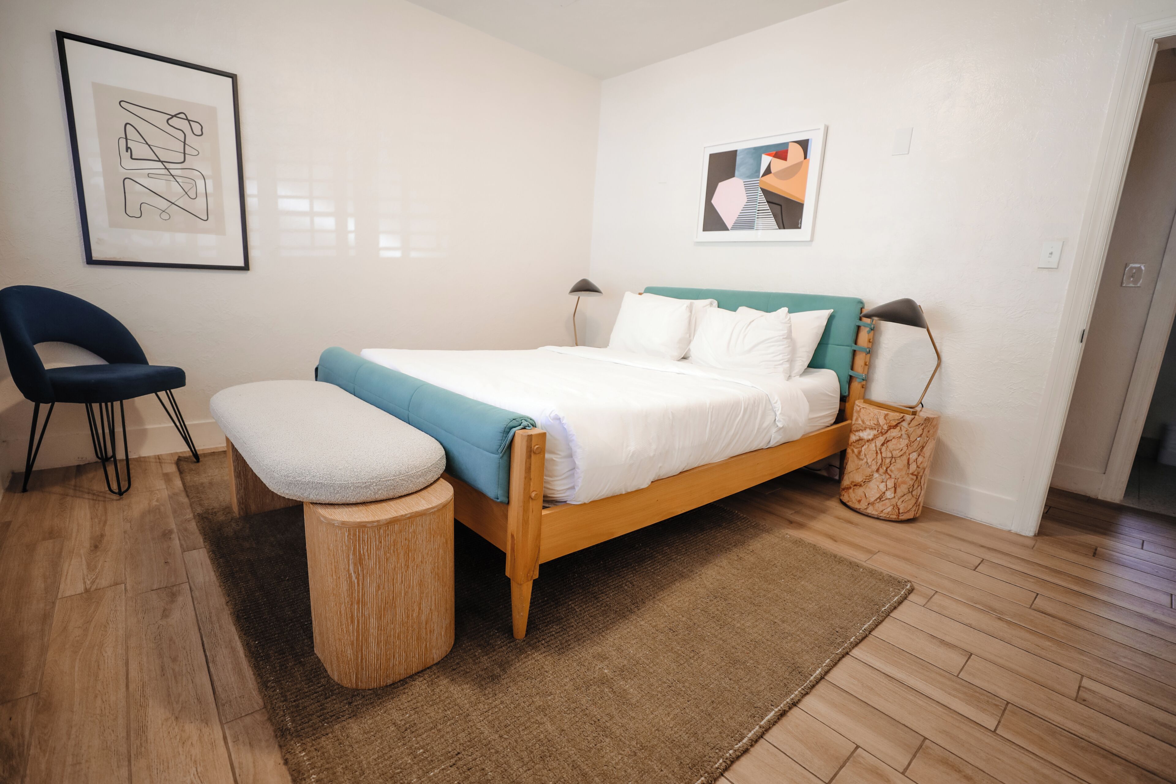 A bedroom with a bed, a chair, a bedside table, a lamp, and a wall-mounted picture.