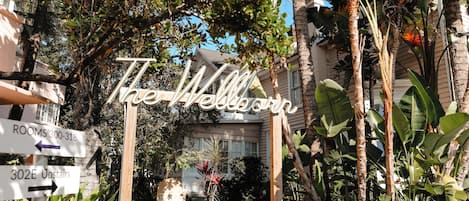 Un letrero con la leyenda 'The Wellborn', rodeado de abundante follaje y un edificio al fondo.