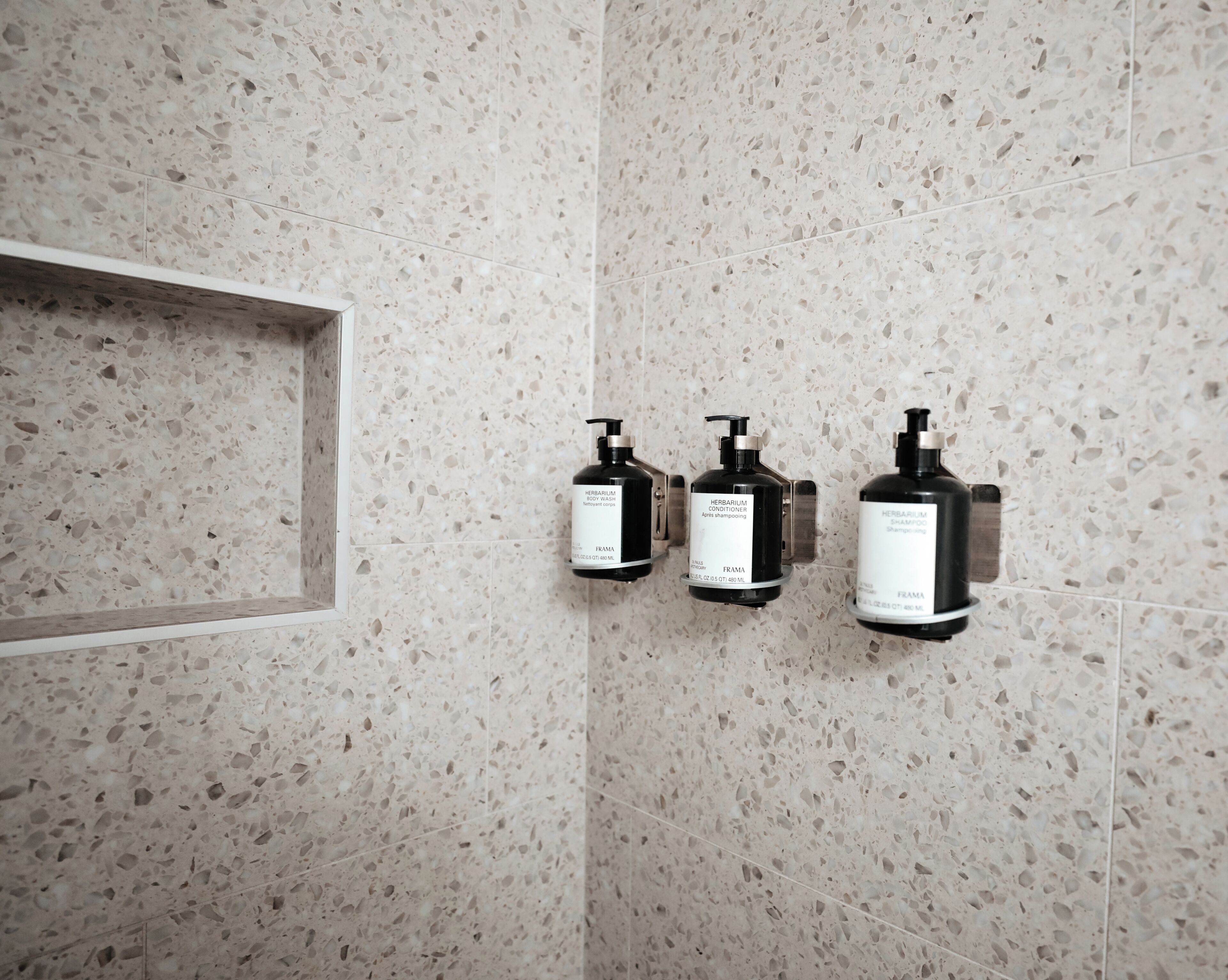 A bathroom with a speckled tile wall and three black dispensers mounted on it.