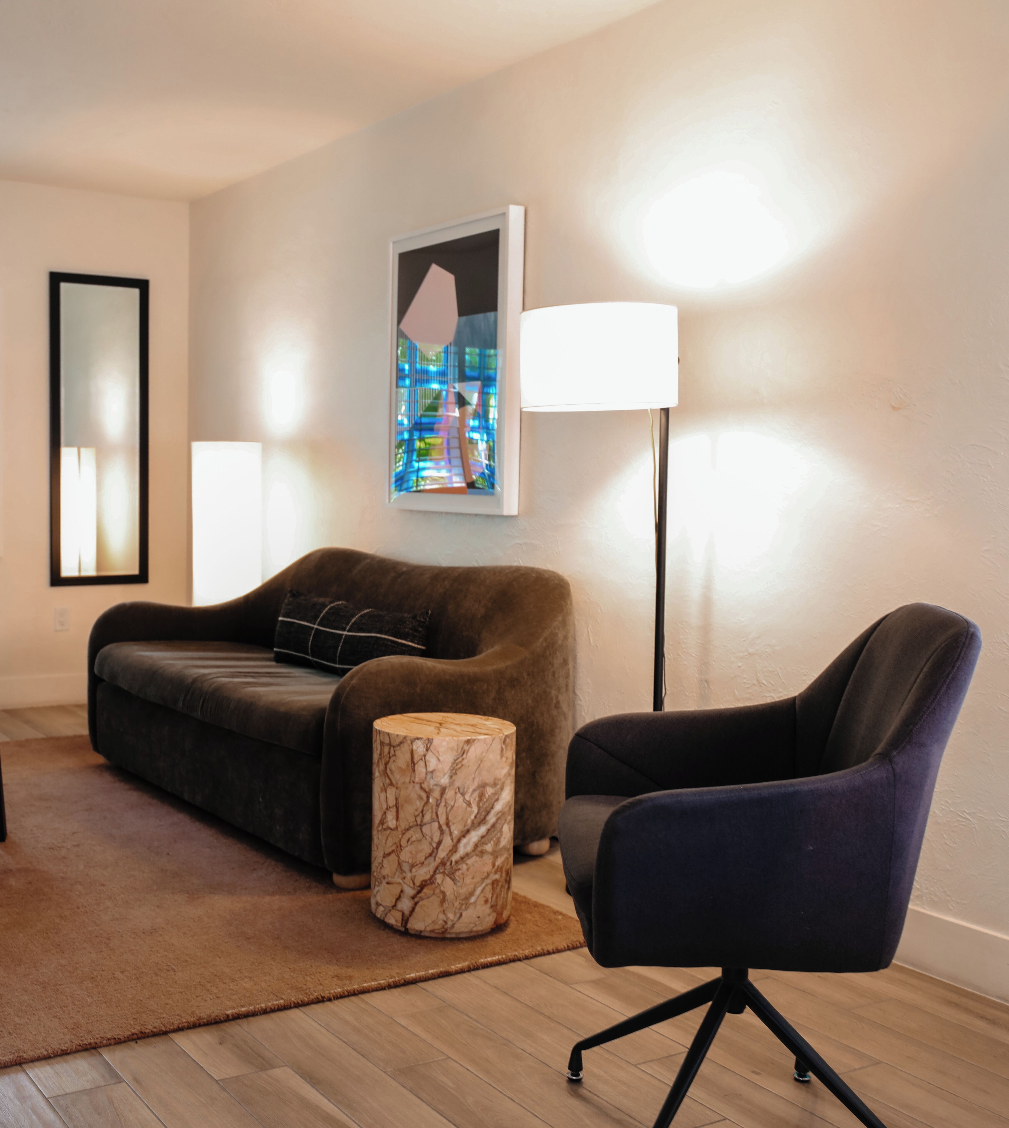 Een moderne woonkamer met een donkerbruine bank, een ronde marmeren salontafel, een zwarte bureaustoel en een vloerlamp.