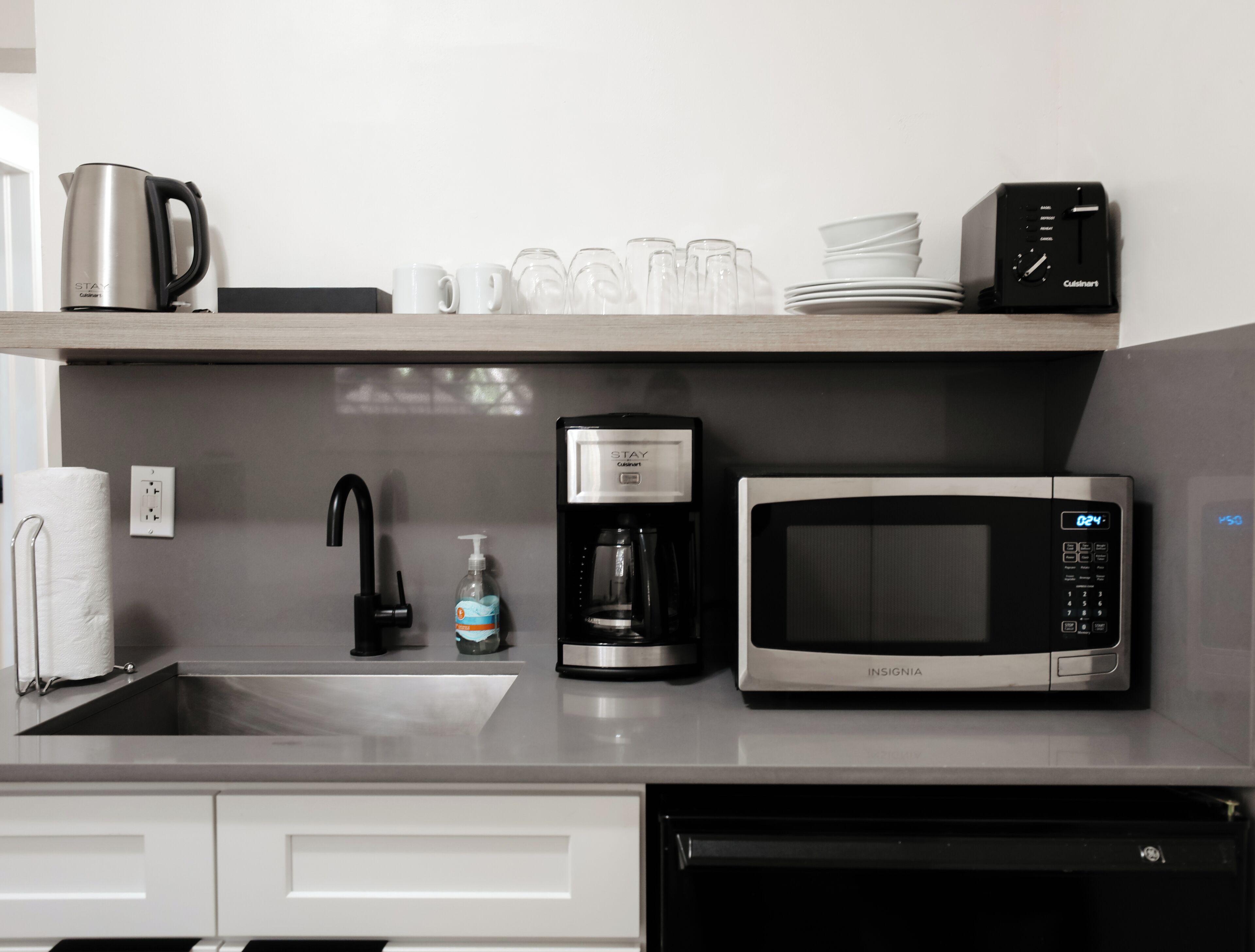 A kitchen with a coffee maker, microwave, and a dish rack with cups and plates.