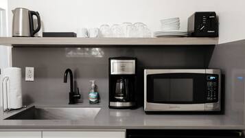 A kitchen with a coffee maker, microwave, and a dish rack with cups and plates.