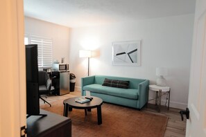A living room with a teal sofa, a coffee table, a TV, a lamp, and a framed abstract artwork on the wall.